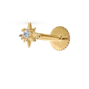 May include: Gold star-shaped stud earring with a small clear gemstone in the center. The earring has a post and a butterfly backing.