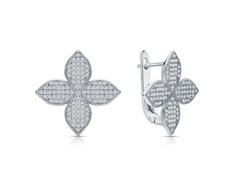 May include: A pair of silver-toned earrings shaped like four-petaled flowers. Each petal is covered in small, clear, sparkling stones. One earring is shown from the front, while the other is angled to reveal the hinged clasp mechanism.