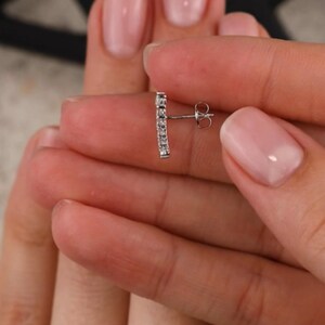 May include: A silver earring with a row of small, clear cubic zirconia stones set in a bar shape. The earring has a post and butterfly back.