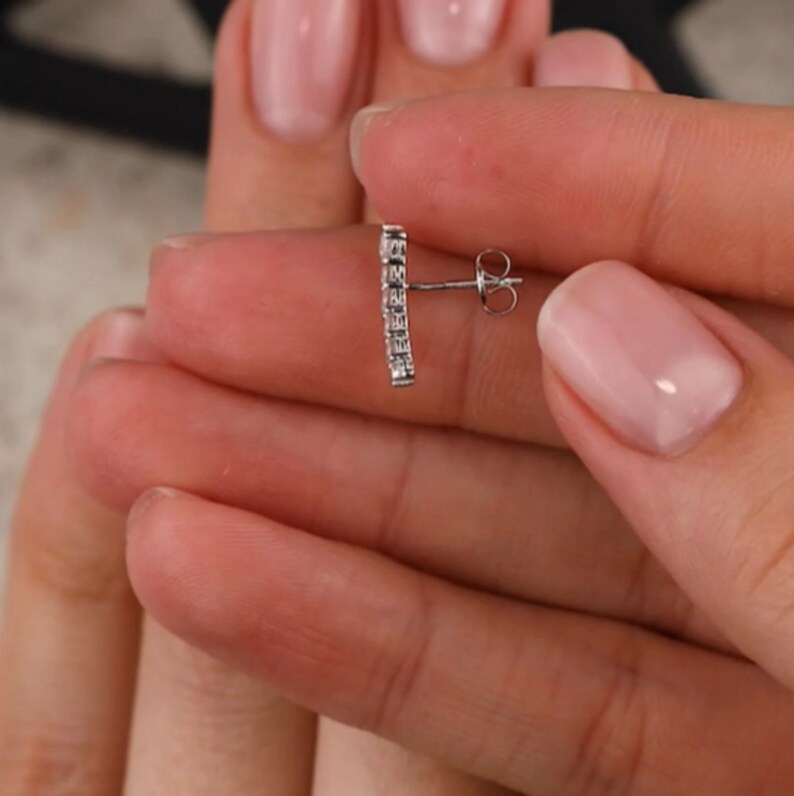 May include: A silver earring with a row of small, clear cubic zirconia stones set in a bar shape. The earring has a post and butterfly back.