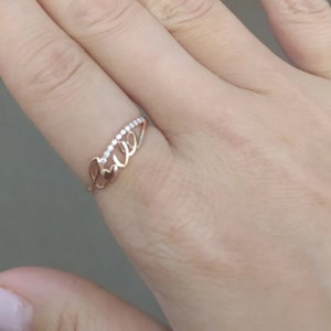 May include: A rose gold ring with the word "Love" spelled out in cursive with small diamonds set along the top of the band.