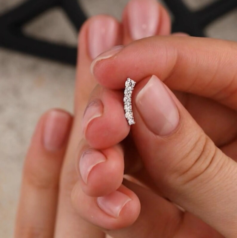 May include: A curved bar earring with a row of small, clear, round gemstones.