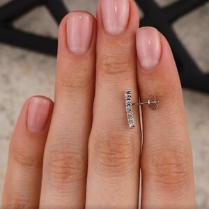 May include: A silver earring with a row of small, clear cubic zirconia stones set in a curved bar design.