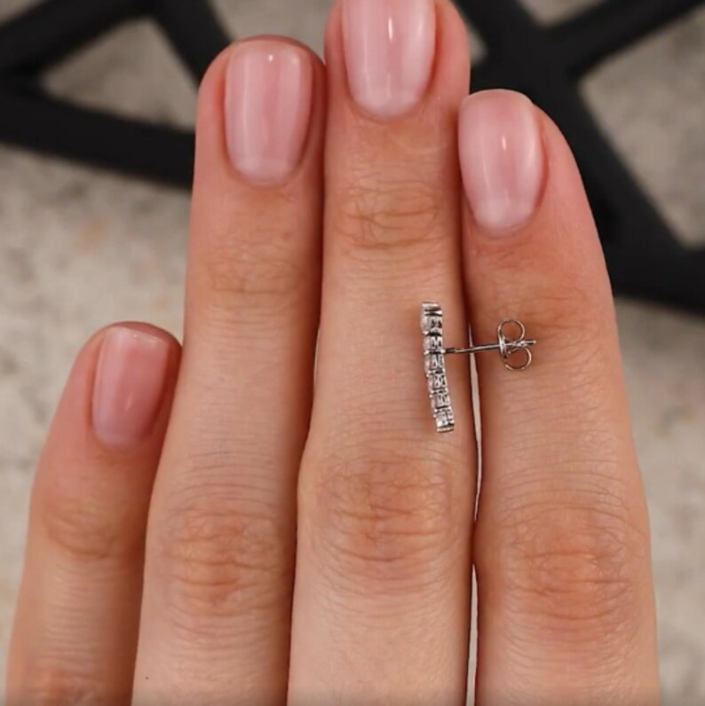 May include: A silver earring with a row of small, clear cubic zirconia stones set in a curved bar design.