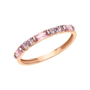 Puede incluir: Un anillo de banda en oro rosa con una serie de piedras preciosas rosas alternas. El diseño incluye dos piedras rosas rectangulares de corte baguette en los extremos y dos piedras rosas de corte redondo en el centro, engastadas en garras plateadas.