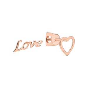 Könnte beinhalten: Ein Paar Ohrringe aus Roségold. Ein Ohrring zeigt das Wort "Love" in einer kursiv geschriebenen Schrift. Der andere Ohrring ist eine einfache Herzform mit einem offenen Zentrum.