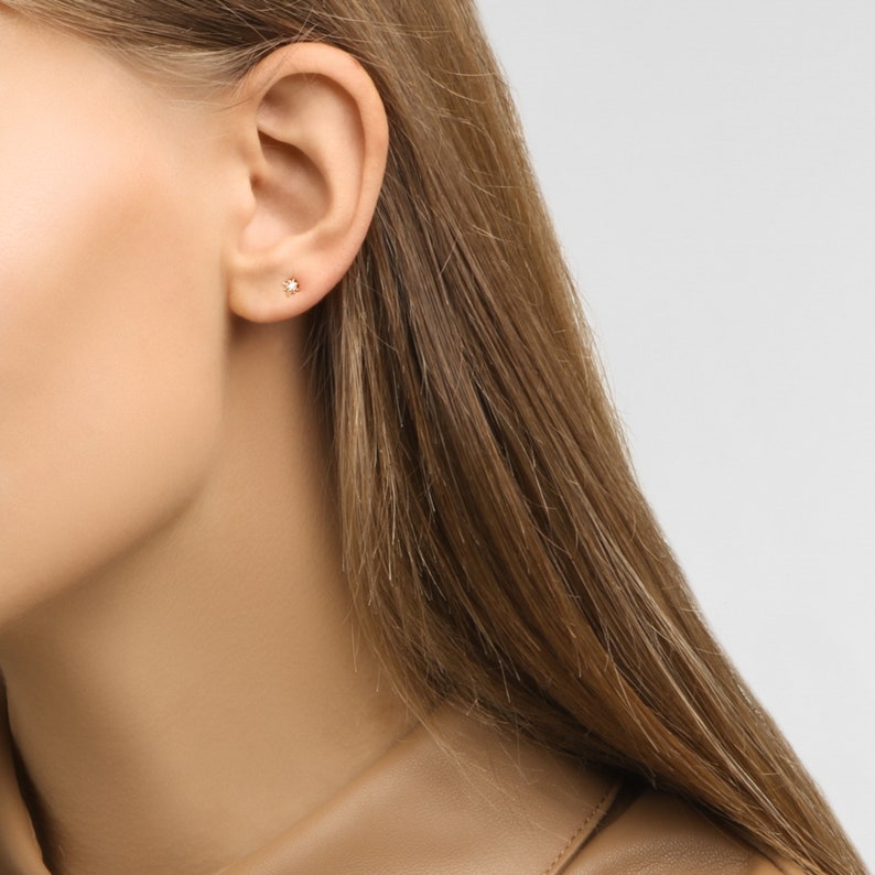 May include: A close-up of a woman's ear with a small, gold star-shaped earring with a clear stone in the center.