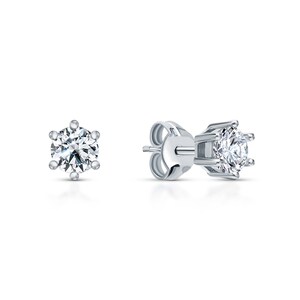 May include: A pair of silver stud earrings with a round, clear gemstone in the center.