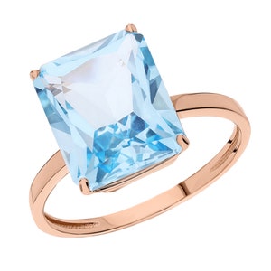 Puede incluir: Un anillo de oro rosa con una gran piedra preciosa cuadrada de color azul claro.