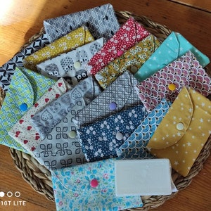 Peut inclure: Une collection de pochettes en tissu colorées avec différents motifs et designs. Les pochettes sont disposées en cercle sur une surface en bois. Certaines pochettes ont des boutons ou des pressions. Une barre de savon blanche est au centre du cercle.
