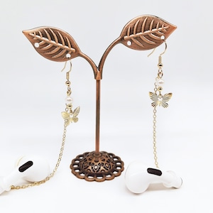 May include: A pair of gold butterfly earrings with pearl accents hanging from a leaf-shaped stand. The earrings are on a gold chain.