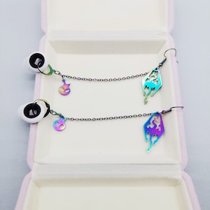 May include: A pair of iridescent earrings with a chain and a star charm. The earrings are in a white box with a pink interior.