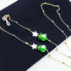 May include: Two gold chains with green and white glass beads and charms. The charms are shaped like stars and turtles. The chains are attached to a clear plastic loop.