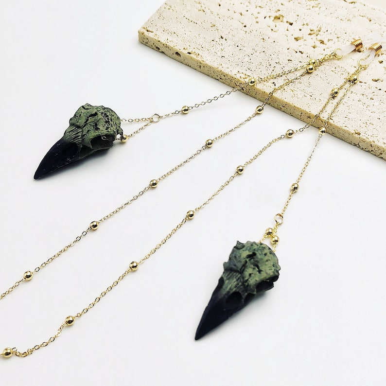 May include: A pair of gold chain glasses retainers with green and black bird skull charms.