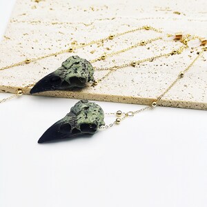 May include: A pair of long, gold chain necklaces with green and black bird skull pendants. The chains have small gold beads.