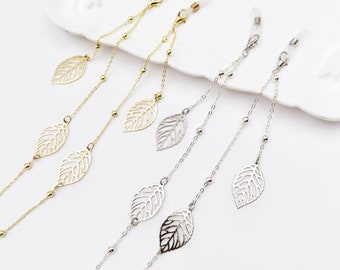 May include: Three pairs of gold, silver, and black eyeglass chains with leaf-shaped charms. The chains are made of metal and have small beads.