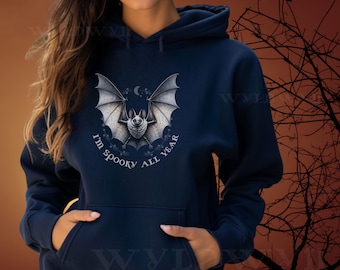 May include: Navy blue hooded sweatshirt featuring a detailed bat graphic with outstretched wings, a crescent moon, and the text "I'm spooky all year." The design is centered on the front of the sweatshirt, which has a kangaroo pocket.