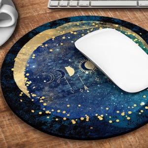Könnte beinhalten: Eine runde Mauspad in Blau und Gold mit einem himmlischen Design mit Monden, Sternen und einer Sonne. Auf der Mauspad liegt eine weiße Computermaus.
