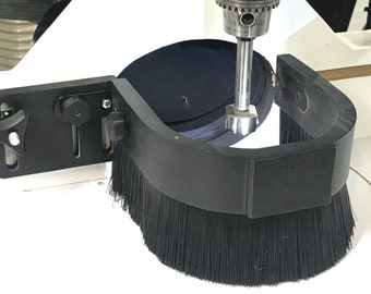 May include: A black brush attachment for a router, with the brand name "Nelson" printed on the side. The brush is attached to a white surface with a black metal bracket.