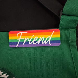 May include: A green apron with a rainbow-colored name tag that says "Friend" in white text.