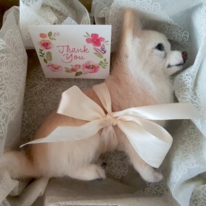 May include: A handcrafted dog figurine in light colours, presented in a decorative box with a cream-coloured bow. A small card with floral details and the words "Thank You" is included. The dog has a fluffy texture.