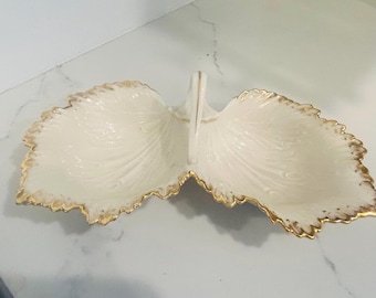 May include: A white porcelain serving dish shaped like two leaves with a gold trim. The dish has a handle in the center.