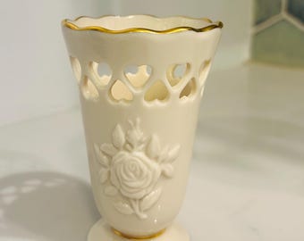 May include: A small, white porcelain vase with a gold trim. The vase has a cut-out design of hearts and a raised design of a rose.