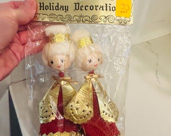 May include: Vintage Christmas ornaments in a clear plastic package. The ornaments are doll-like figures with blonde hair, gold crowns, and red and gold dresses. The package reads "Holiday Decoration."