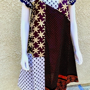 May include: A patchwork dress with a navy blue, white, and gold floral print. The dress has a scoop neck and short sleeves. The dress is made of cotton and is perfect for summer.