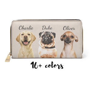 May include: A beige zippered wallet with three dogs on it. The dogs are a yellow lab, a pug, and a chihuahua. The dogs are labeled 'Charlie', 'Duke', and 'Oliver'. The text '16+ colors' is below the dogs.