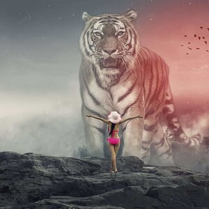 Puede incluir: Una mujer con un bikini rosa y un sombrero blanco se para con los brazos extendidos frente a un gran tigre blanco con rayas negras. El tigre está de pie en un acantilado rocoso con un fondo brumoso. El cielo es un degradado de rojo y gris.