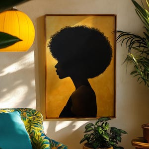 Può includere: Una stampa artistica incorniciata con una silhouette nera di una persona con afro su sfondo dorato. L'opera è esposta su una parete bianca, completata da una lampada a sospensione gialla e piante in vaso, creando un'atmosfera calda.
