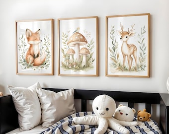 May include: Three framed watercolor prints featuring woodland animals. The prints include a fox, mushrooms, and a deer, all surrounded by greenery. The frames are made of light-colored wood. The prints are displayed above a bed with pillows and stuffed animals.