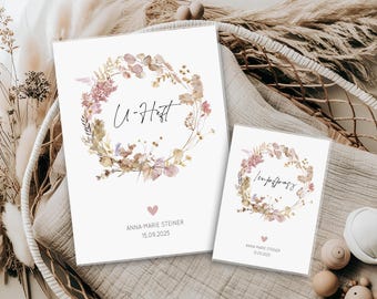 Könnte beinhalten: Zwei weiße Karten mit floralen Kranzdesigns. Die größere Karte hat den Text "U-Heft" und die kleinere Karte den Text "Impfpas". Beide Karten enthalten einen Namen und ein Datum. Weiche, neutrale Farben und ein Herz.