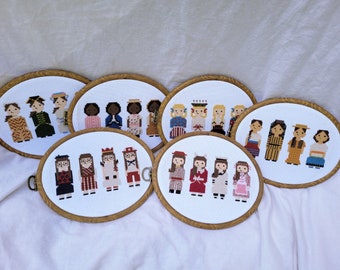 May include: Five embroidery hoops with cross-stitch designs of women in various outfits. The hoops are arranged in a semi-circle on a white fabric background.