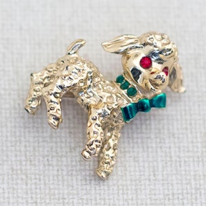 May include: Gold-tone brooch of a poodle with red rhinestone eyes and a green bow tie.