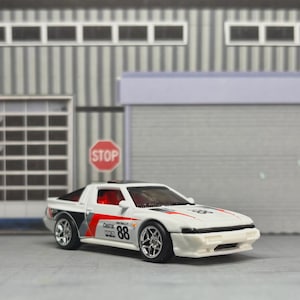 Könnte beinhalten: Ein weißes Modellauto aus Druckguss mit roten und schwarzen Rennstreifen, der Nummer 88 an der Seite und Castrol-Schriftzug. Das Fahrzeug hat ein schwarzes Dach, silberfarbene Räder und ein durch die Fenster sichtbares Interieur.