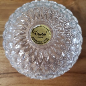 May include: A clear glass bowl with a textured surface. The bowl has a gold label that reads "GARANTI PLUS DE 24% DE PLOMB Cristal FRANCE ECHT BLEIKRISTALL 24% PBO GENUINE LEAD CRYSTAL".