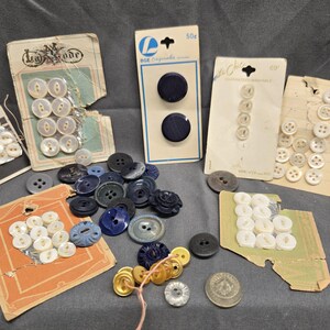 May include: Assortment of buttons in various colors and sizes, including white, blue, and gold. Some buttons are on cards with text, such as "Le Mode" and "DGE Conquirable 50c".