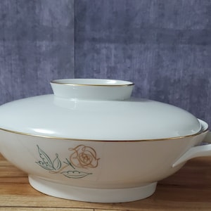 May include: White porcelain serving bowl with a lid, featuring a gold trim and a delicate floral design with a single rose and leaves.