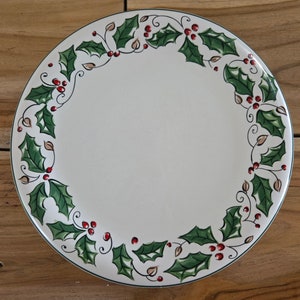 May include: A white ceramic plate with a green and red holly leaf design around the rim.