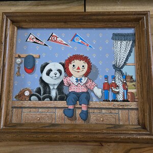 May include: Framed artwork featuring a panda bear and a Raggedy Ann doll sitting side-by-side. The background includes baseball pennants, a baseball glove, a cap, and toy soldiers. The artwork is signed by C. Carson.