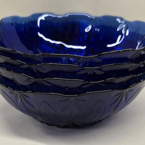 May include: A stack of four cobalt blue glass bowls. Each bowl has a scalloped rim and a leaf pattern etched into the glass. The bowls are nested together, showcasing their depth and design.