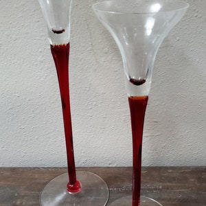 May include: Two tall, clear glass candle holders with red stems and round bases.