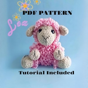 May include: A handmade pink crochet lamb with a fluffy texture, sitting on a light blue background. The lamb has beige accents on its face, ears, and feet. Text on the image reads "PDF PATTERN", "Lea", and "Tutorial Included".