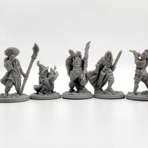 Może przedstawiać: Pięć szarych miniaturowych figurek fantasy, w tym czarodziej, wojownik i łucznik, ustawionych w rzędzie. Każda figurka jest szczegółowa z unikalnym pancerzem i bronią, stojąc na indywidualnych okrągłych podstawach. Figurki są ustawione na gładkim białym tle.