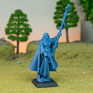 Op de afbeelding: Een blauwe plastic miniatuurfiguur van een persoon die een gewaad draagt en een staf met een vlam erop vasthoudt. Het figuur staat op een zwarte basis.
