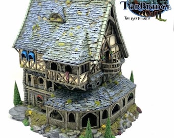 Könnte beinhalten: Ein detailliertes Miniatur-Fantasy-Haus mit grauem Ziegeldach, Holzbalken und Steinakzenten. Das Haus verfügt über mehrere Ebenen, Balkone und Bogenfenster. Der Text "Torbridge" und "The Last Hearth" sind sichtbar.