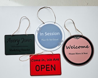 May include: Four different signs with twine hangers. The signs are green, blue, red, and pink. The green sign says "Avery Jones Marketing Director". The blue sign says "In Session Please Do Not Disturb". The red sign says "Come in, We Are OPEN". The pink sign says "Welcome Please Have A Seat".