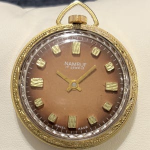 Reloj de bolsillo colgante NAMRUF vintage de 17 joyas, fabricado en Suiza, con detalles ornamentados en tono dorado.